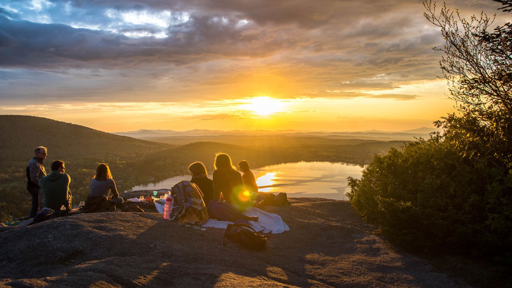 Menschen auf einem Berg vor einem See in der Abendsonne 