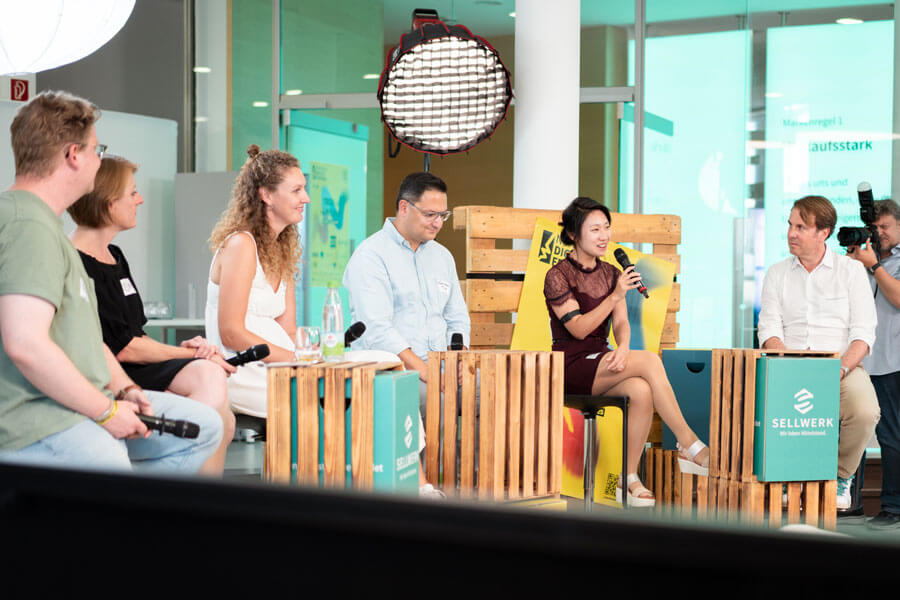 Sechs Personen sitzen auf Holzpaletten-Stühlen im Halbkreis mit Mikrofonen, hinter ihnen ein großes Licht und ein Nürnberg Digital Festival Logo.