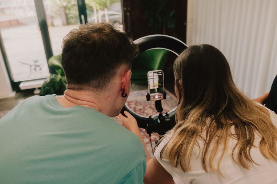 Zwei Personen betrachten gemeinsam ein Smartphone, das in einem Ringlicht befestigt ist, von hinten fotografiert.