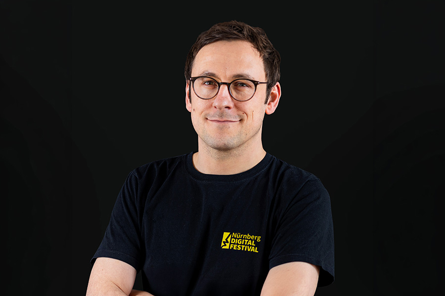 Man in a black shirt with glasses smiling and looking to the side.