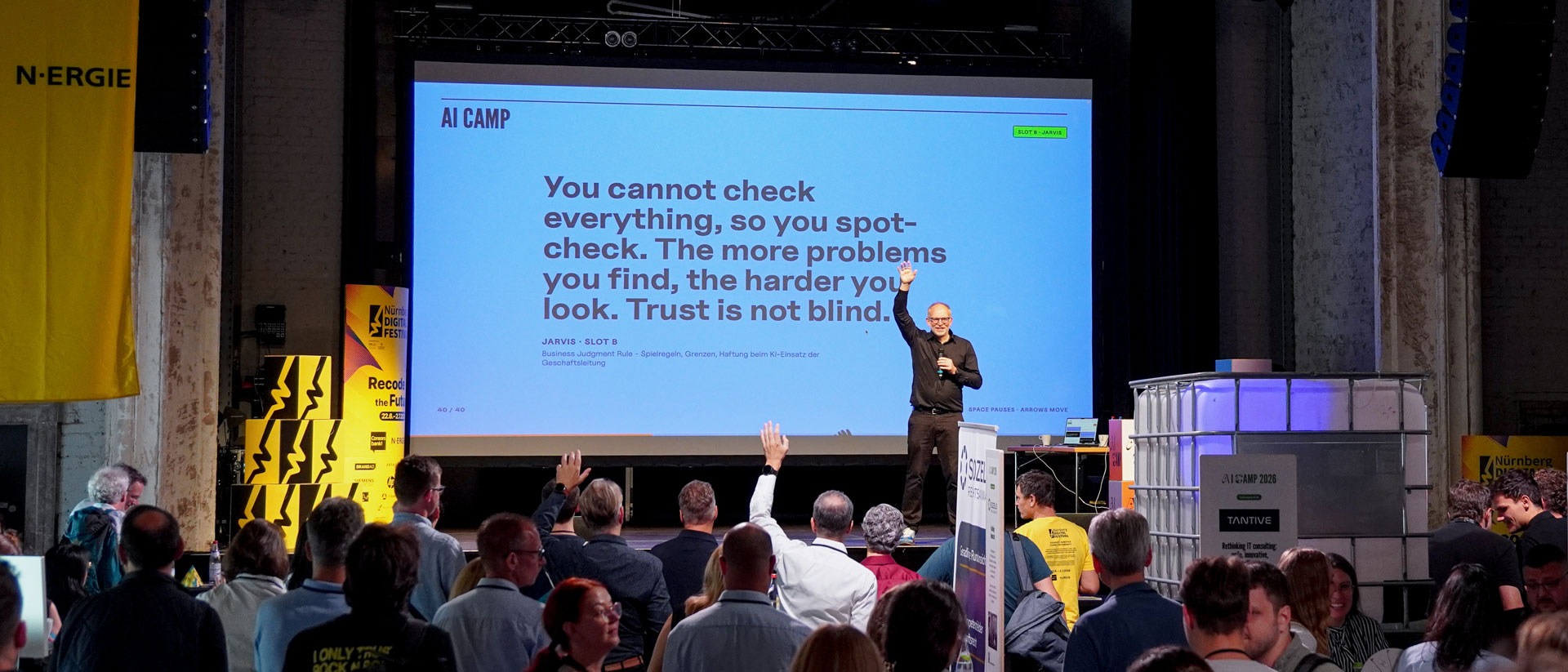 Redner hebt vor Publikum die Hand; Leinwand zeigt „You cannot check everything“.