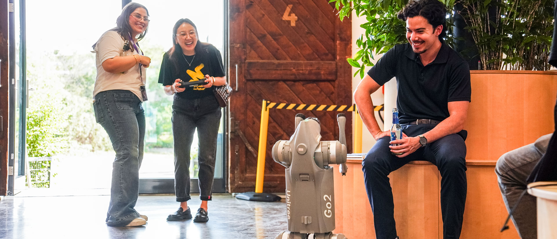Zwei Frauen lachen mit Controller; Mann sitzt neben dem Roboter Go2.