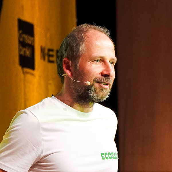 Mann mit Bart und Headset trägt ein weißes T-Shirt mit „ECOSIA“.