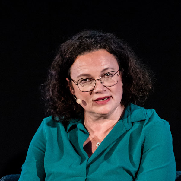 Frau mit Brille und Headset vor schwarzem Hintergrund.